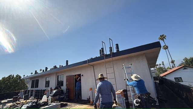 Crew installing low-slope metal roof and fascia on residential building