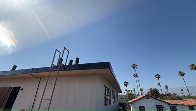 Completed low-slope metal roof and dark fascia on white stucco building