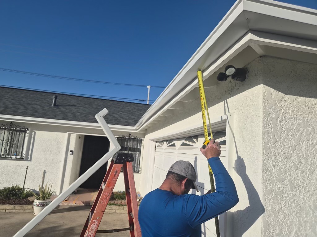 Worker measuring roof eave above garage for white gutter installation