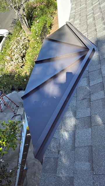 Dark metal bay window roof accent with radial seams over shingle roof