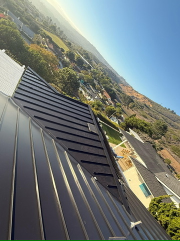 Standing seam metal roof with hillside neighborhood view under clear blue sky