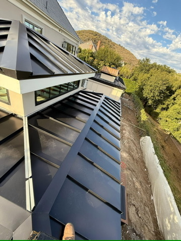 Dark standing seam metal roof along home with hillside backdrop