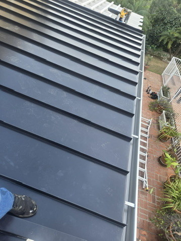 Overhead view of dark standing seam metal roof panels with brick patio below