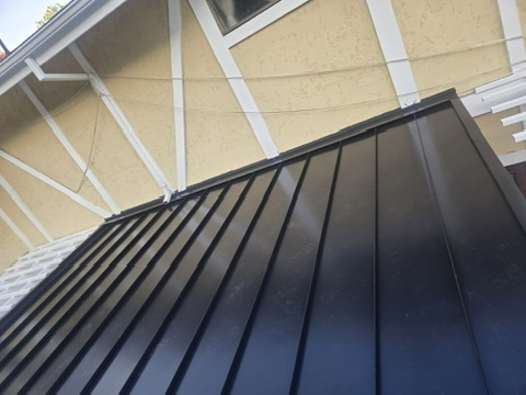 Black standing seam metal roof against yellow stucco home with white trim