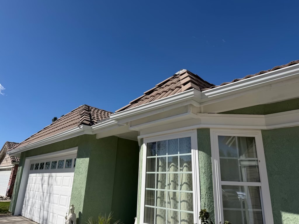 Completed residential tile roof and gutter installation under clear blue sky